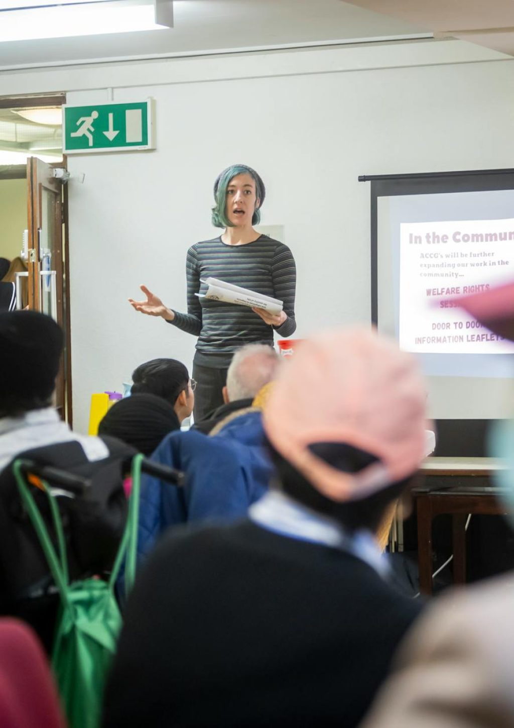 A diverse group attending a community meeting with a presenter speaking in front of a screen.